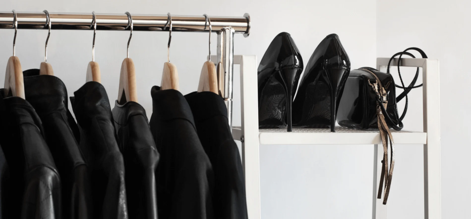 Image of black clothing on wooden hangers and high heeled shoes on a rack