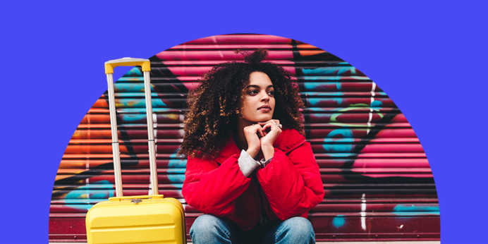 Young woman sitting in front of urban mural with her roller suitcase packed