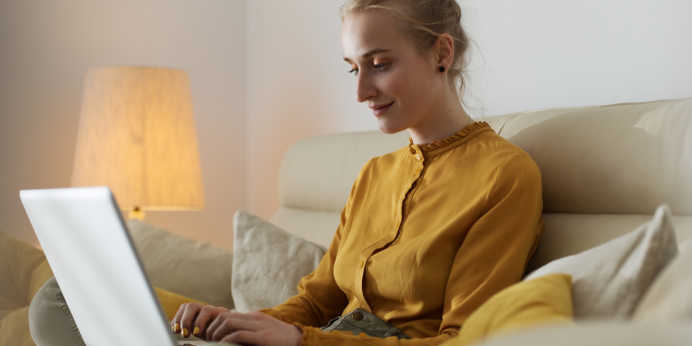 Woman sitting on couch, calmly shopping by using her laptop.