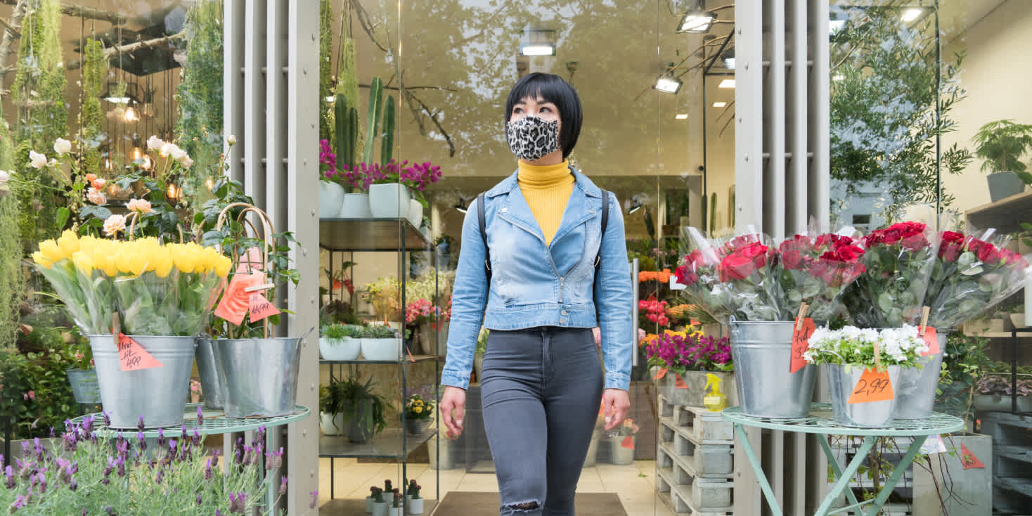 Image of woman shopper with face mask as she leaves a brightly-colored florist shop.