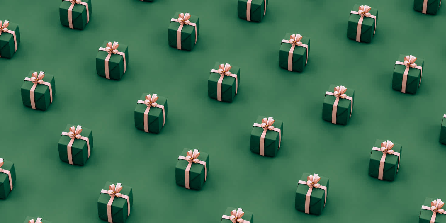 Small gift boxes wrapped in green paper with pink bows arranged in a geometric rows.