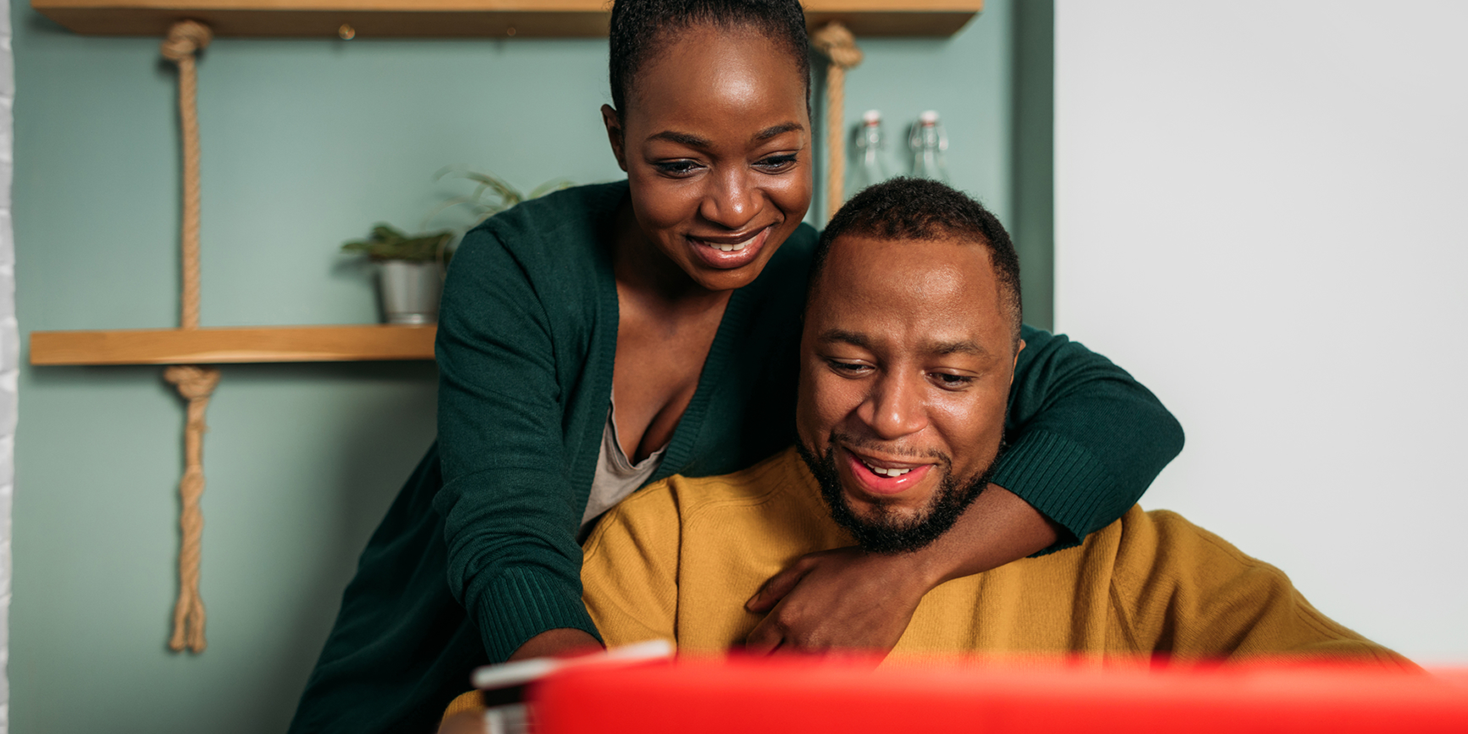 African American married couple enjoying some online shopping together in their dining room.