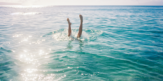 Two legs sticking out of the water mid-dive into a beautiful, tropical sea.