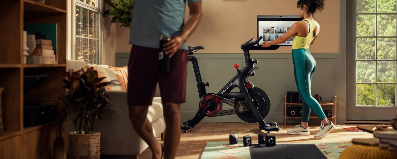 Image of a couple exercising at home using a Peloton bicycle