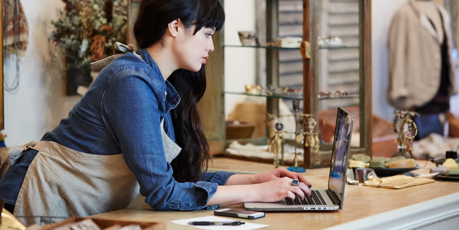 Young female business owner wearing work apron while checking stats on her laptop