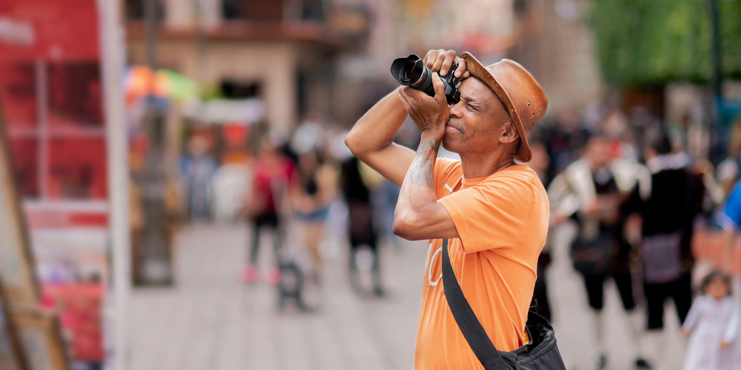 Adult male tourist shooting photographs of a tourist site, with a blurry crowd in the background.