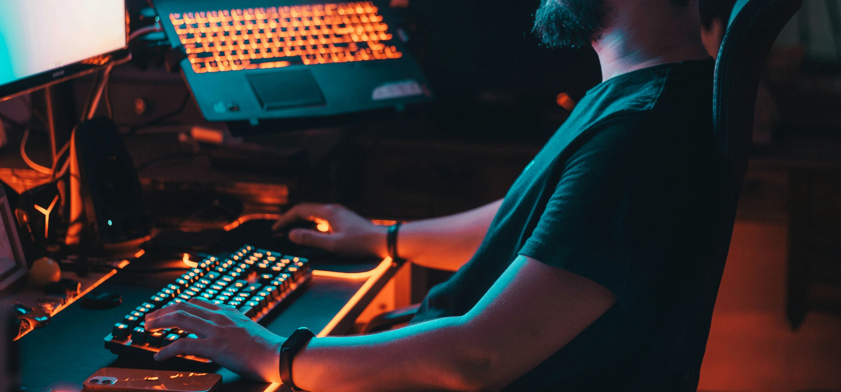 Image of a person sitting at a desk with computer and laptop, glowing orange