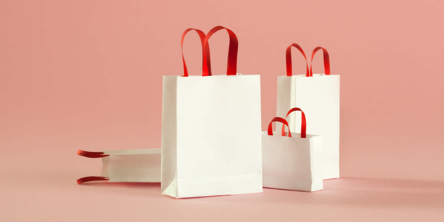 Display of fine white shopping bags with red handles, different sizes.