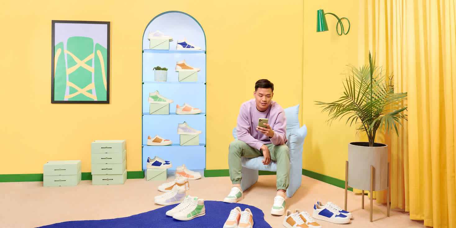 Young man in brightly colored showroom for sneakers, checking his phone and trying on pairs.