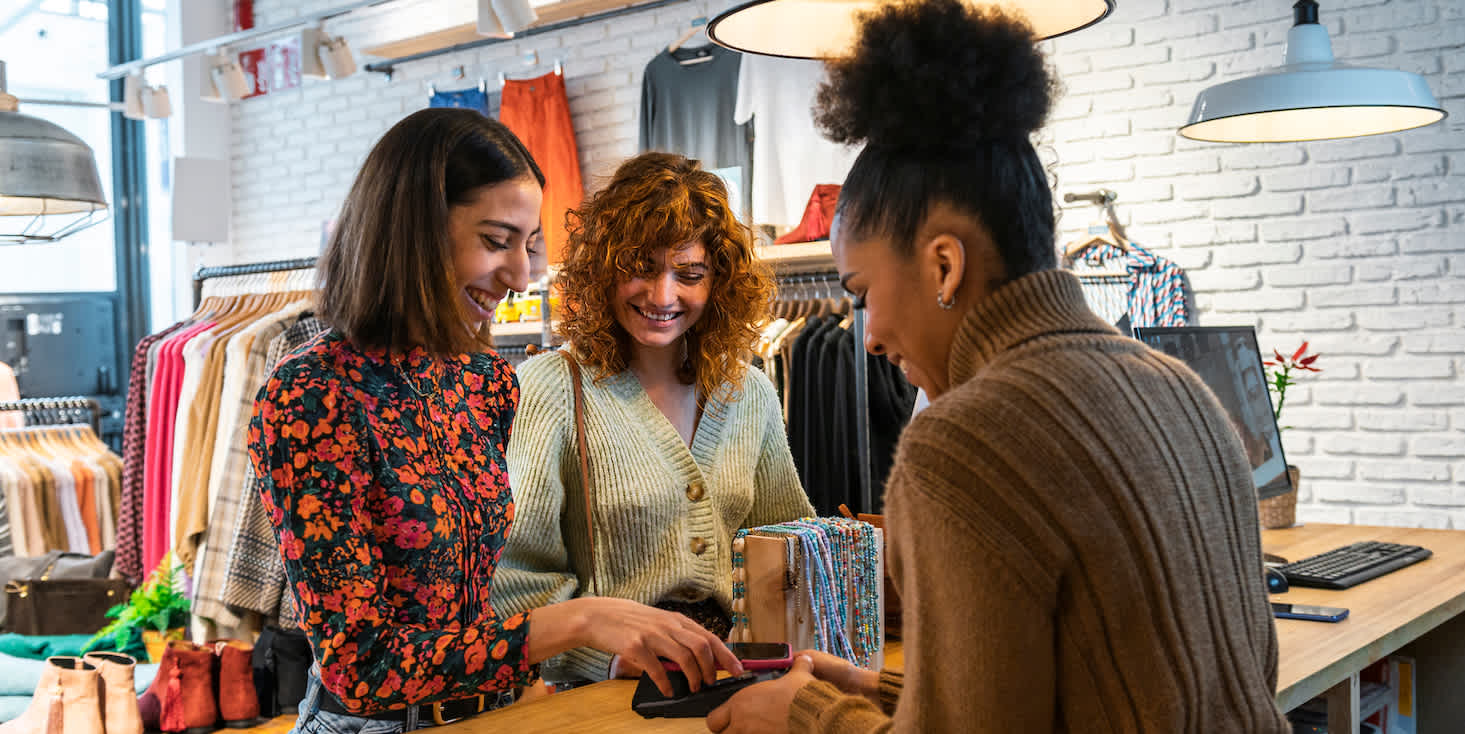 3 women gathered around a sales counter in a clothing boutique checking a detail on a mobile device