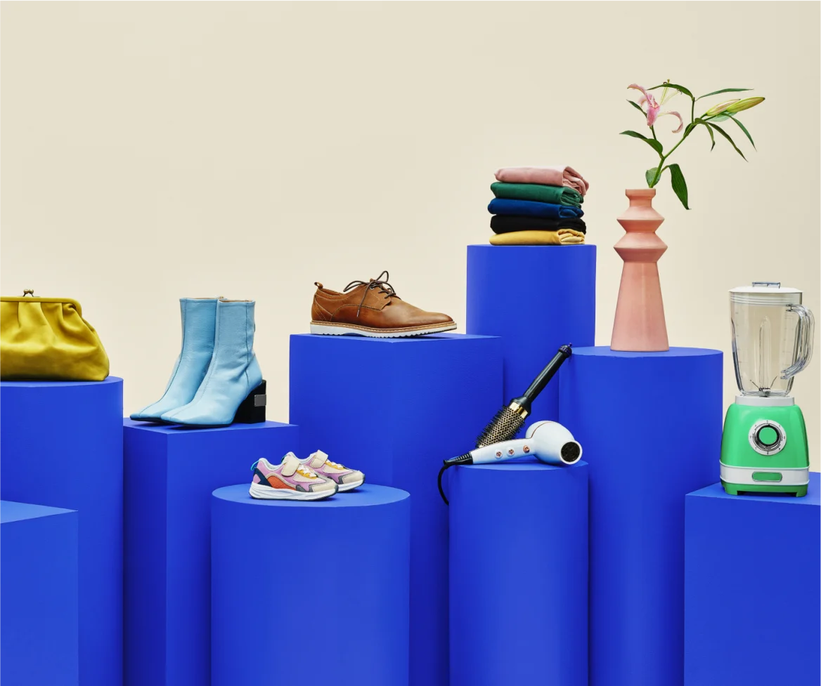 image of shoes, hair dryer, blender, stack of clothes and a potted plant atop blue pedestals, beige background