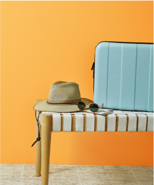 Image of hat, sunglasses and suit case on ottoman. 