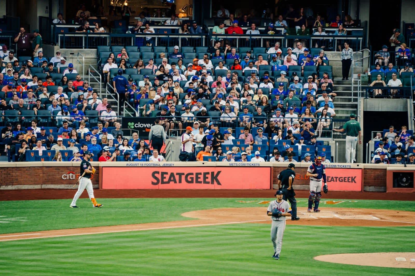 A lively baseball game in progress, with a large crowd of spectators enjoying the match from the stands with a SeatGeek ad.