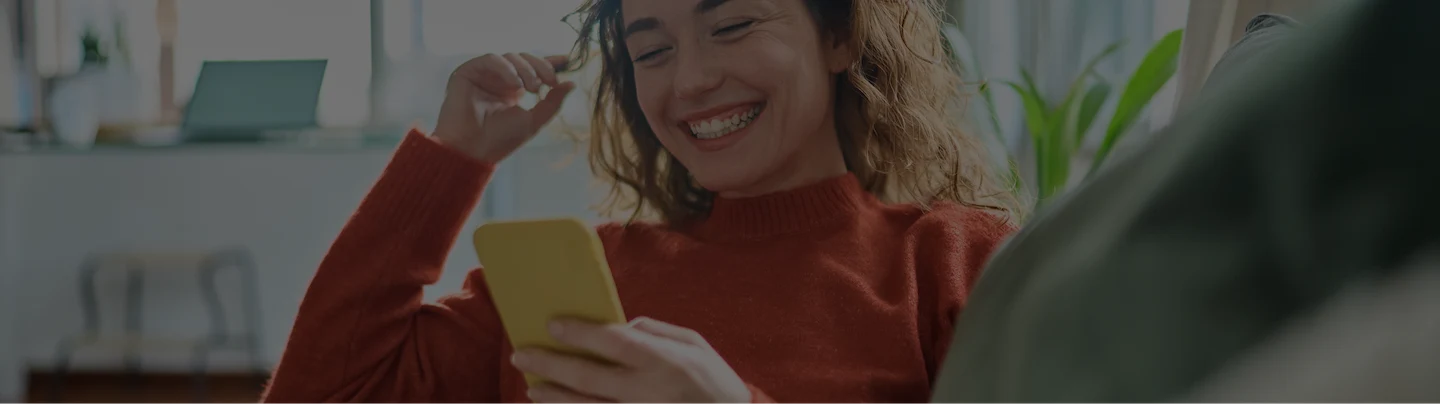 Smiling woman in coral sweater using yellow smartphone for online shopping, representing the seamless Affirm and Google Pay experience