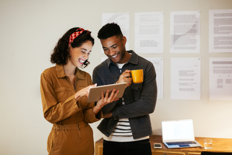 Two people at work looking at an ipad, both are smiling, one is holding a mug 