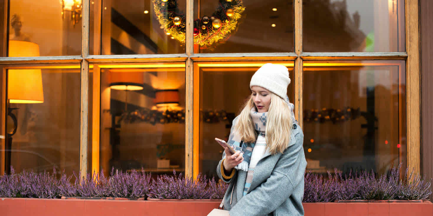 Photo of a young woman outside a hotel/restaurant window while shopping on the Affirm app on her phone