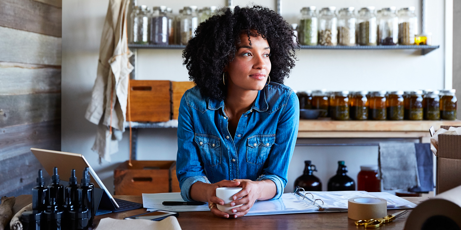 Female business owner in denim shirt enjoying coffee in her studio with a slight smile on her face.