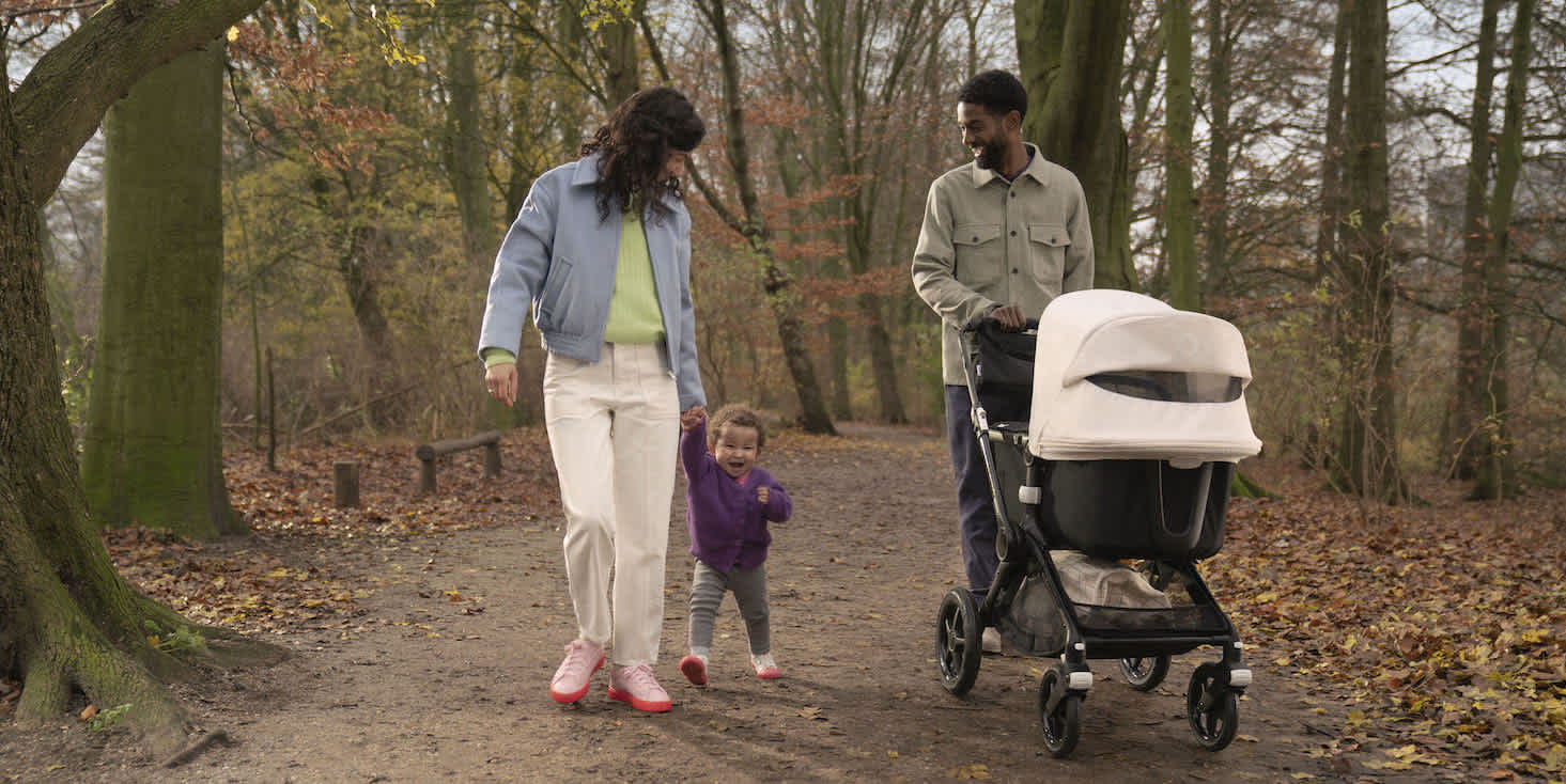 Young couple with toddler and Bugaboo stroller enjoying a walk in the woods during autumn.