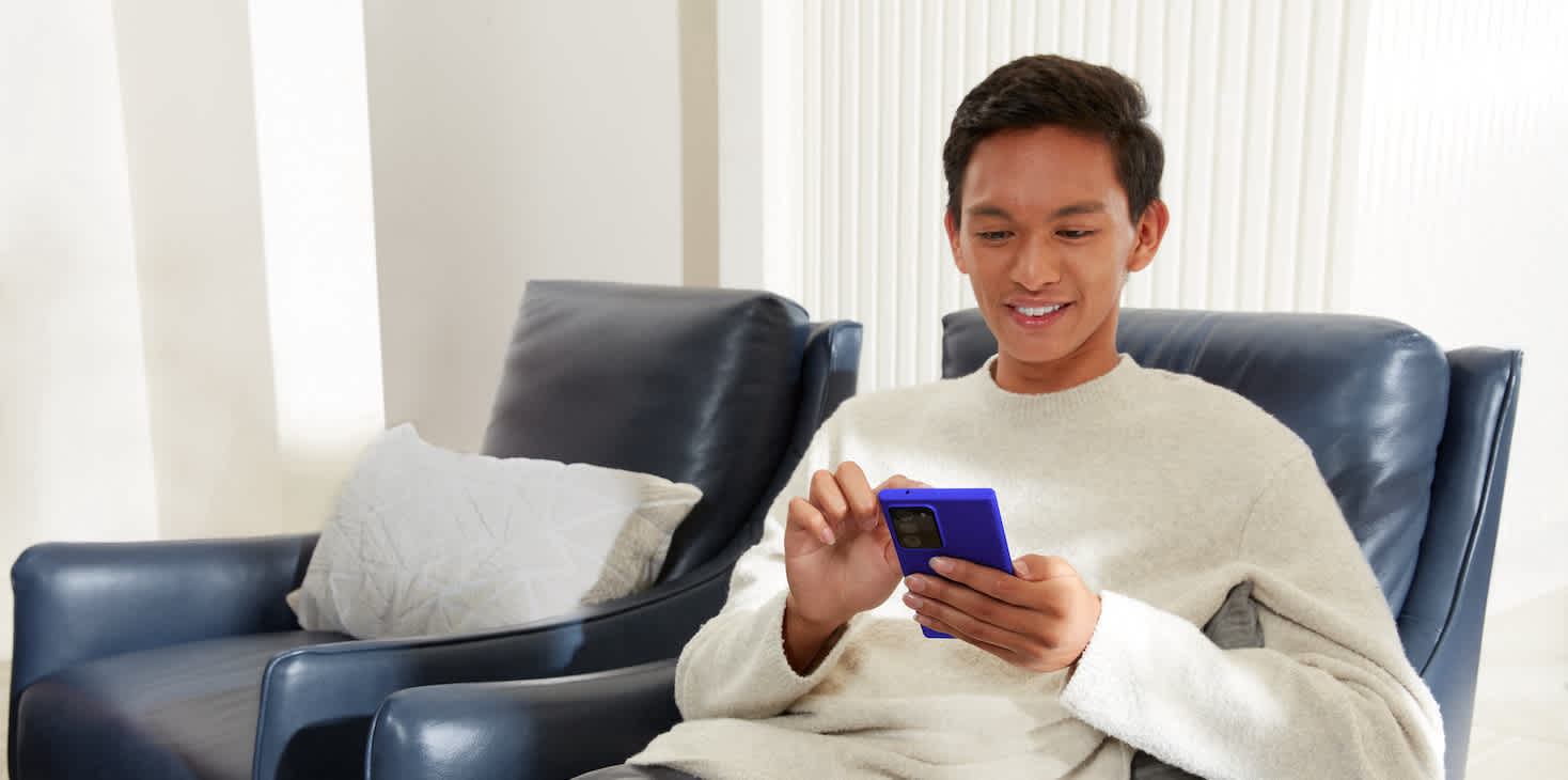 Young man smiling while making a purchase on his phone while sitting in a comfy gray chair