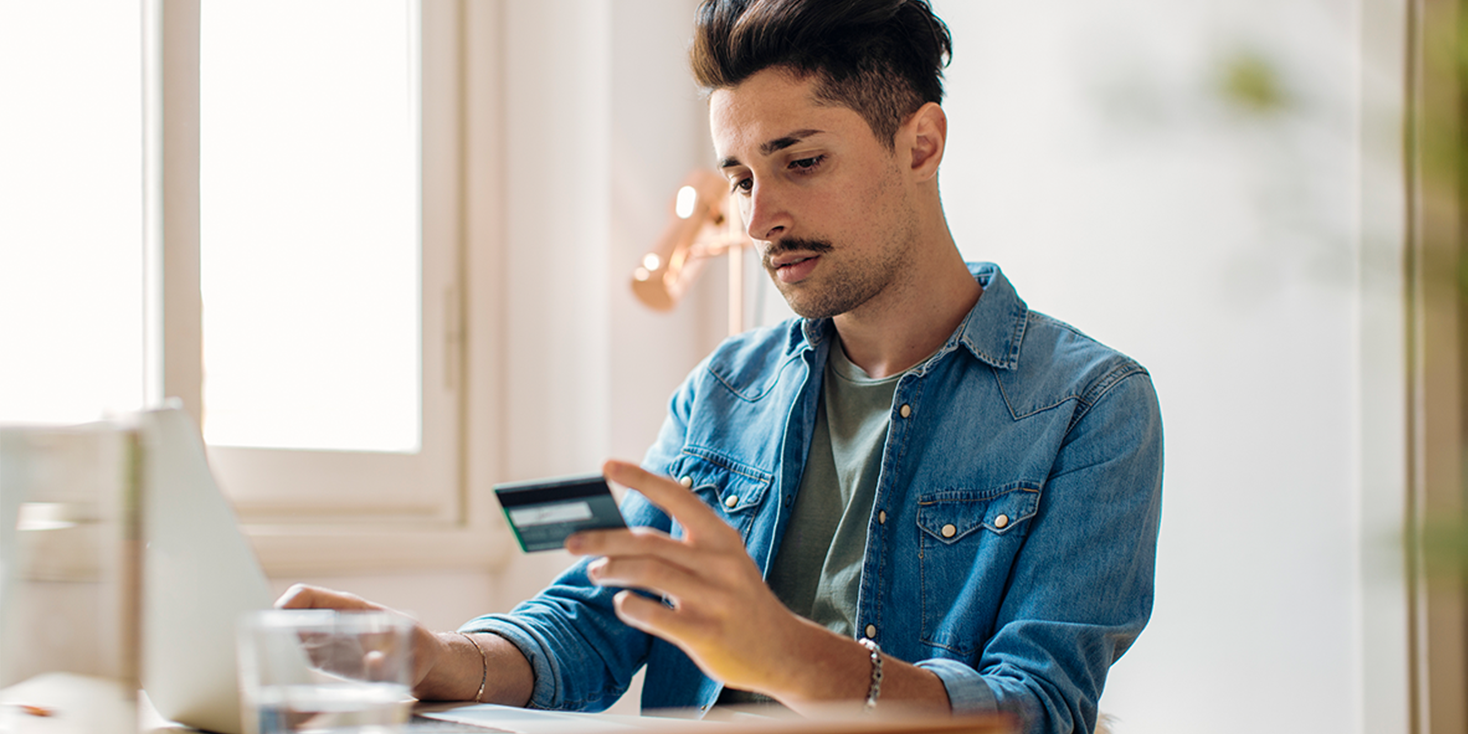 Young man with mustache looking at credit card, getting ready to pay online