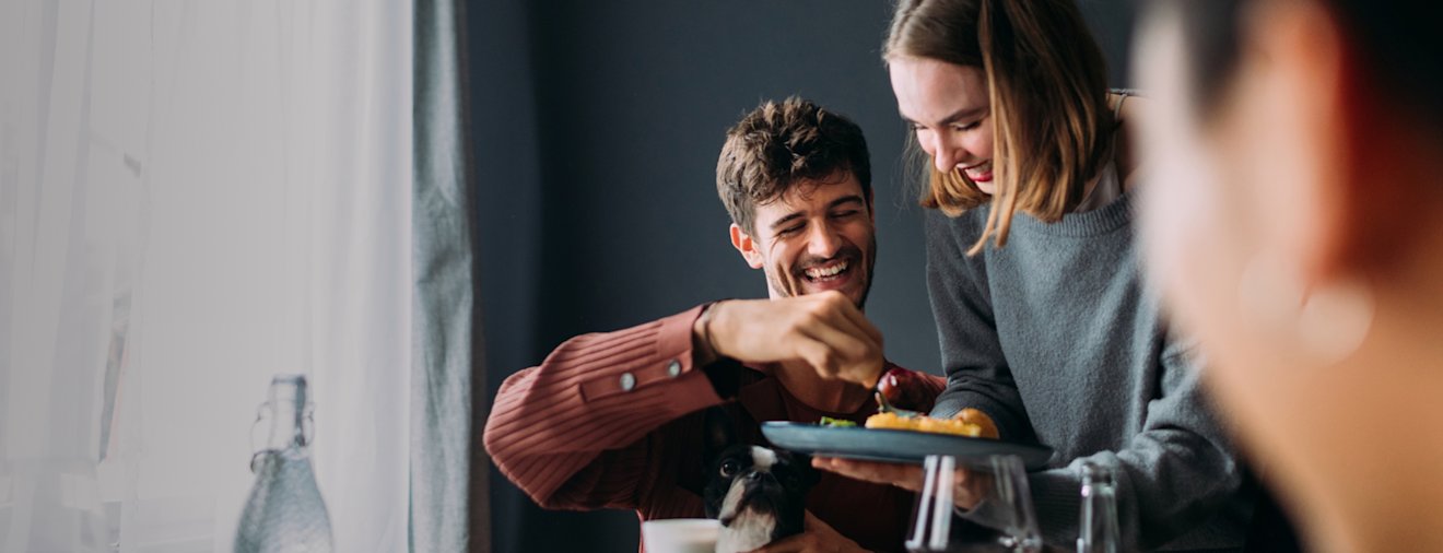 Two people smiling and laughing while sharing food at a dining table with drinks and dishes visible, embodying Affirm's message of "Life on your terms" through joyful social experiences.