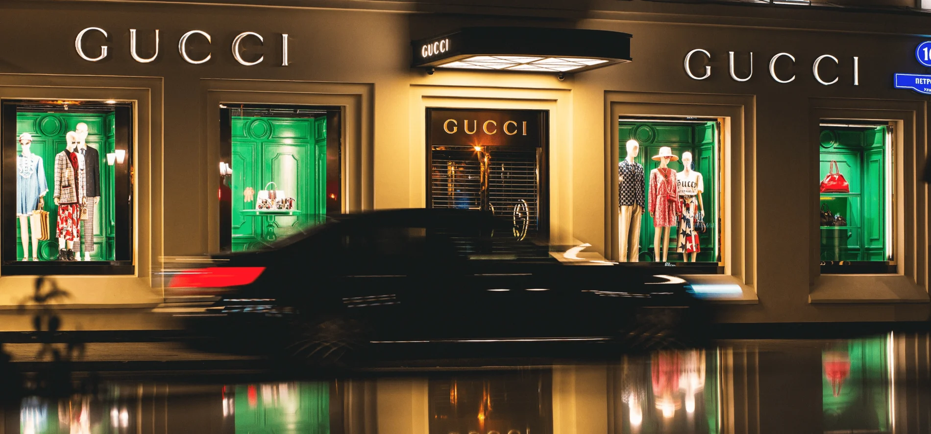 Image of a car passing by in fast motion with a Gucci storefront in the background