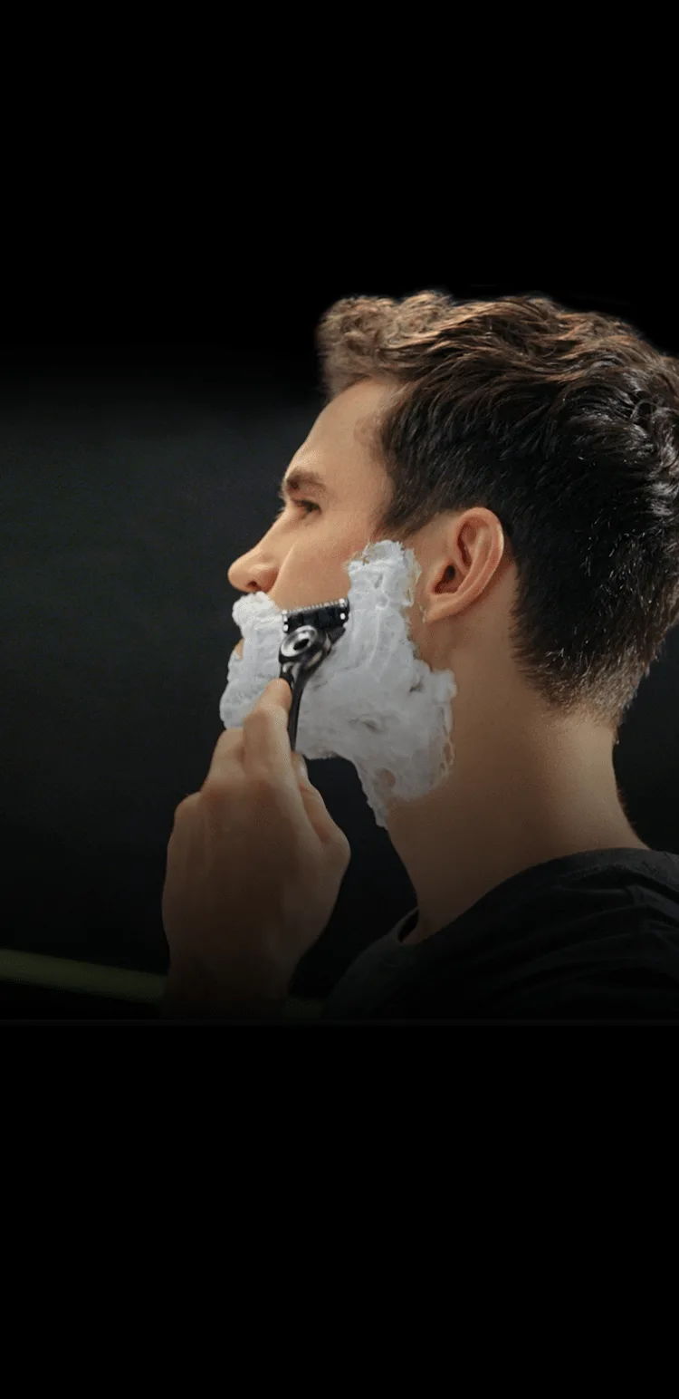 Seitenprofil eines Mannes, der sich mit Rasierschaum das Gesicht rasiert. 