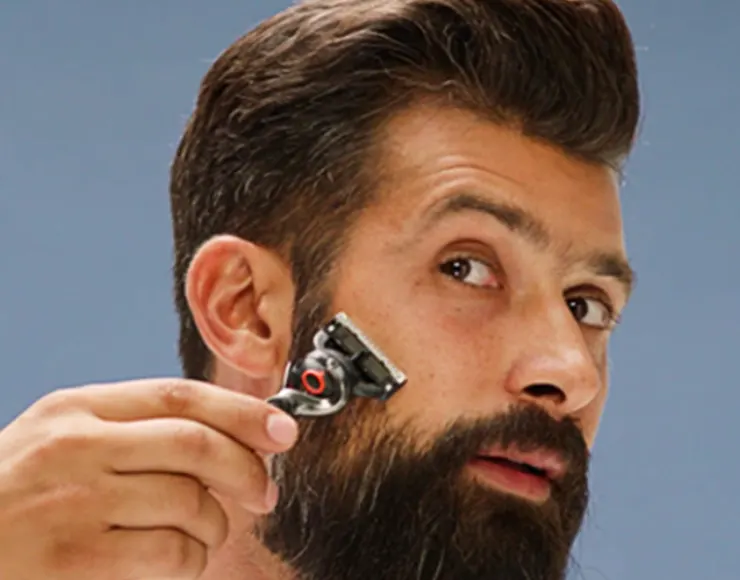 Person styling beard with an razor against a blue background