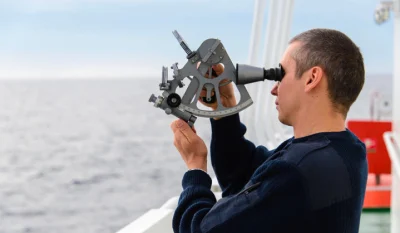 A person appearing to make a noon site with a modern metal sextant on board a ship at sea.