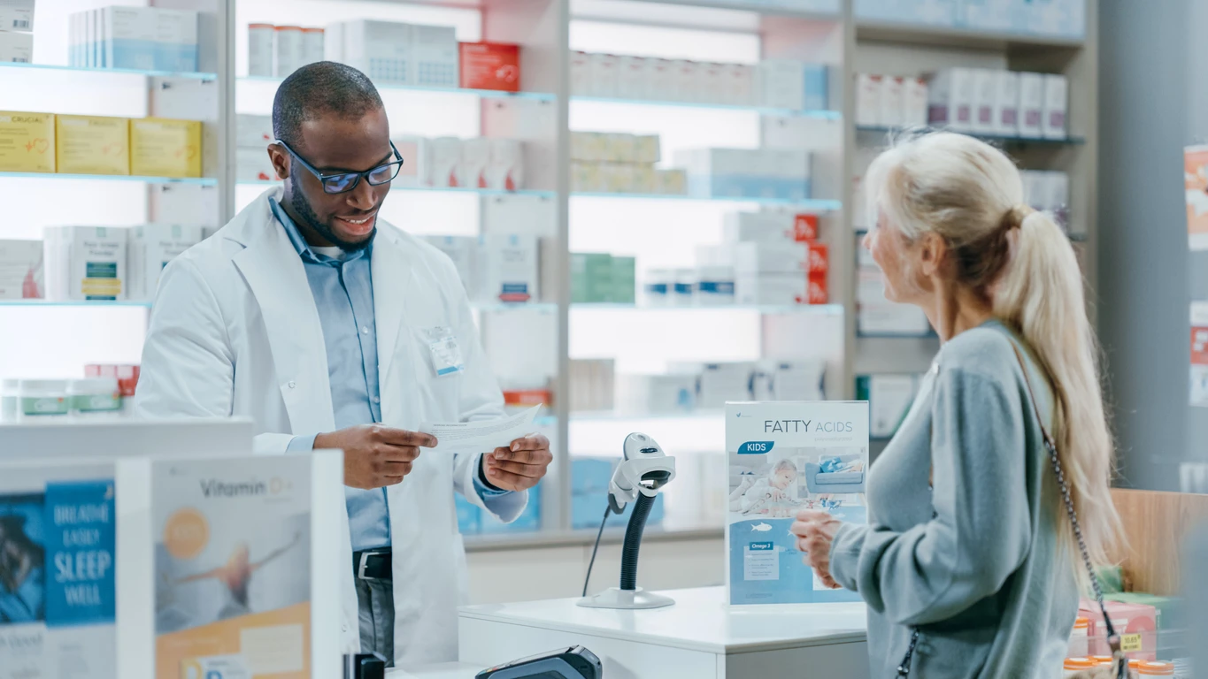 Black male pharmacist at a check out counter advises an older woman with light skin about prescription medication.