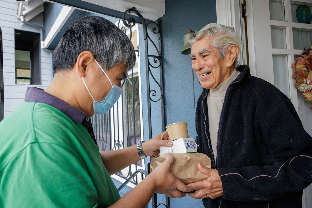 An OnLok staff member wearing a mask brings one of its senior citizens breakfast