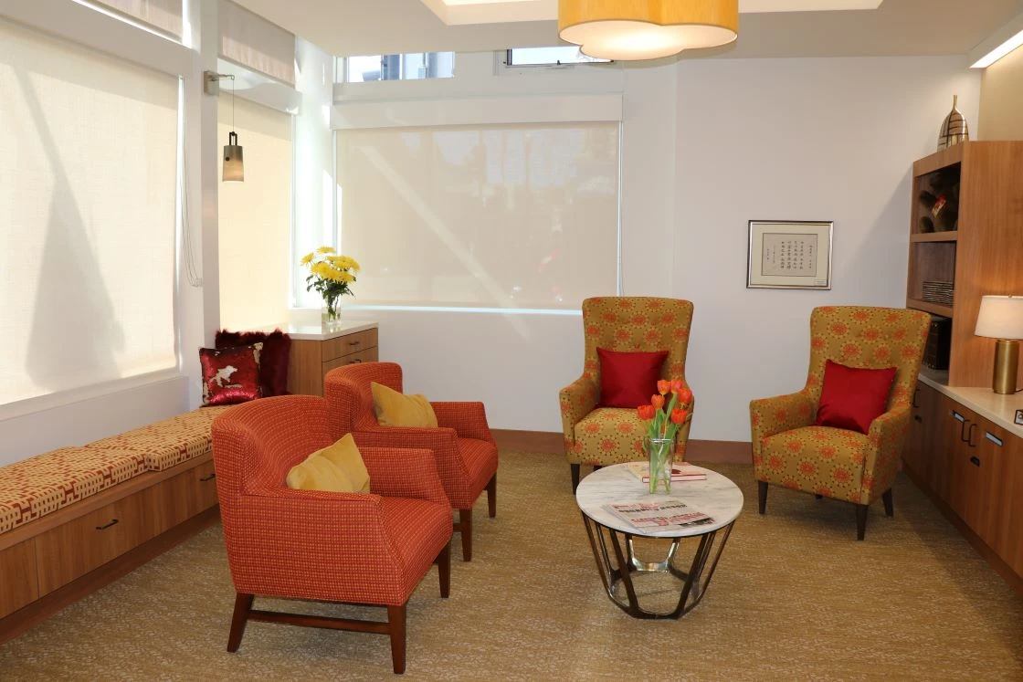 Photo used for the Memory Care Insert. Image features a lounge with two orange chairs on the left side, a round table in the center, and two mustard chairs with circular orange flowers. 