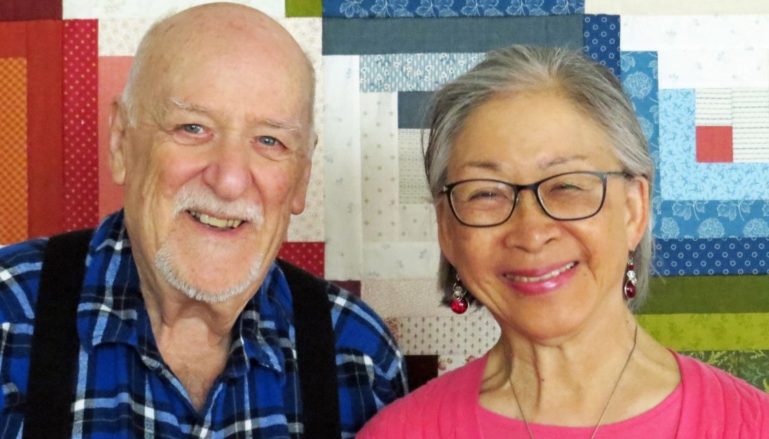 Image of two donors, Charlie and Melody, standing close together with a colorful quilt in the background. 