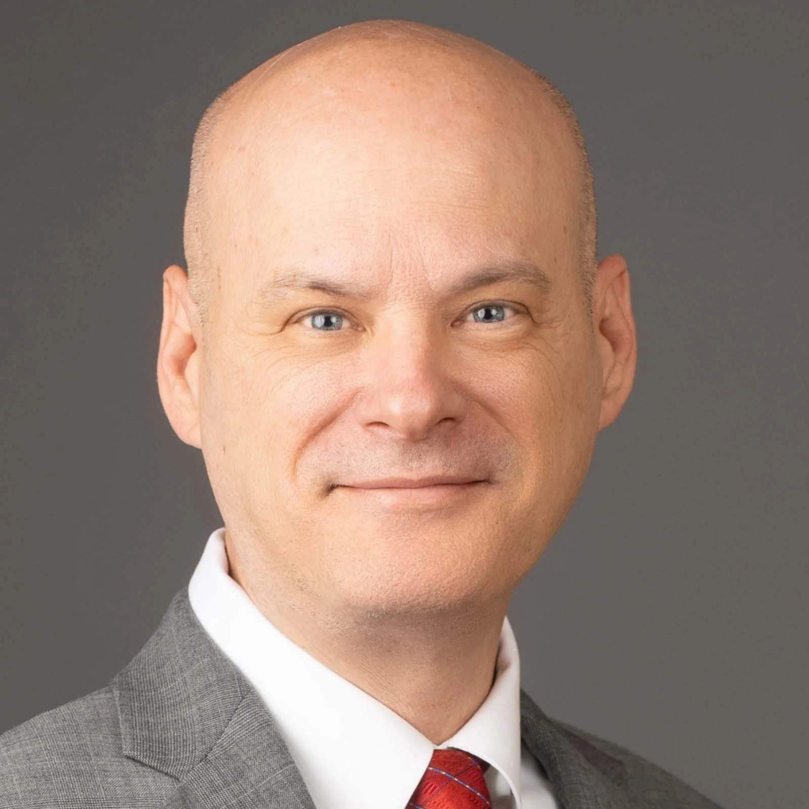 Headshot image of Brian King, CMS Specialist. The background is a dark taupe color. Gary is wearing a light grey blazer, a white button-up shirt, and a red tie. 