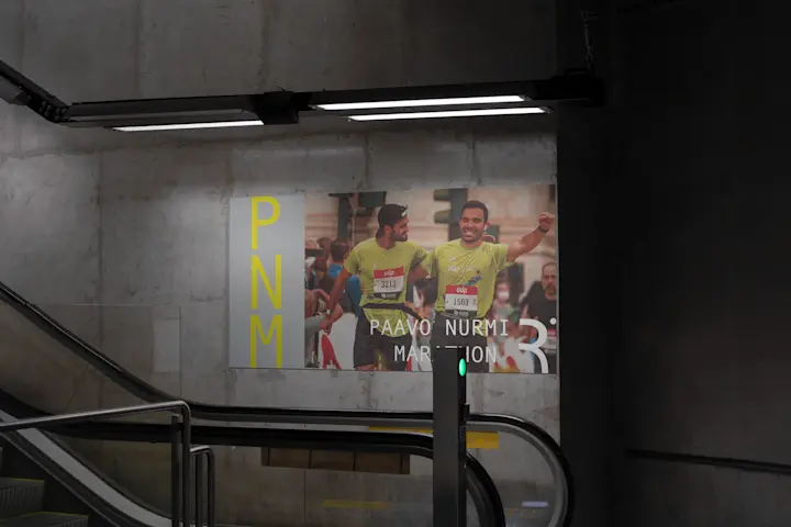 Paavo Nurmi Marathon Subway Advertisement: Underground Passage With Illuminated Paavo Nurmi Marathon Advertisement, Featuring PNM Logo And Runner Image.