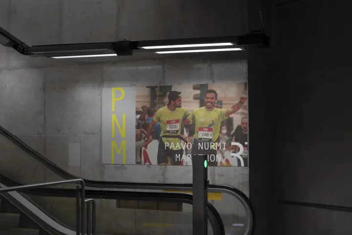 Paavo Nurmi Marathon Subway Advertisement: Underground Passage With Illuminated Paavo Nurmi Marathon Advertisement, Featuring PNM Logo And Runner Image.