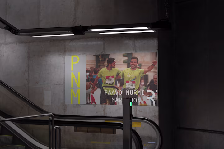 Underground Passage With Illuminated Paavo Nurmi Marathon Advertisement, Featuring PNM Logo And Runner Image.