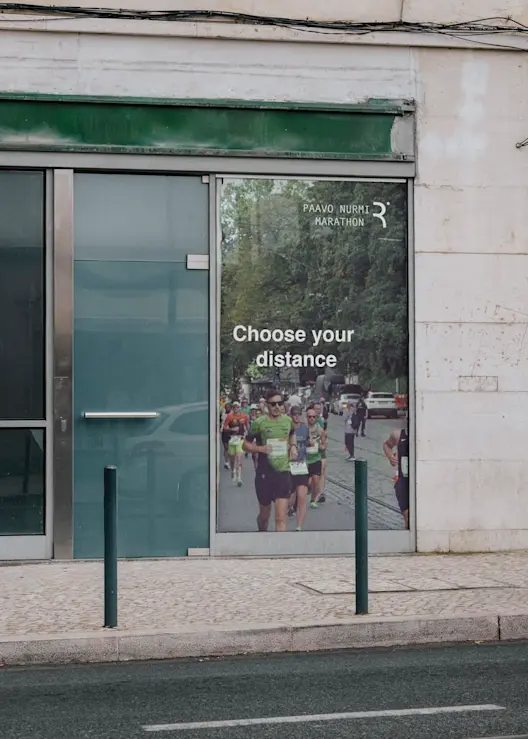 Paavo Nurmi Marathon Urban Advertisement: Digital Billboard In City Street Promoting Paavo Nurmi Marathon, Showing Runners And 'Choose Your Distance' Text.