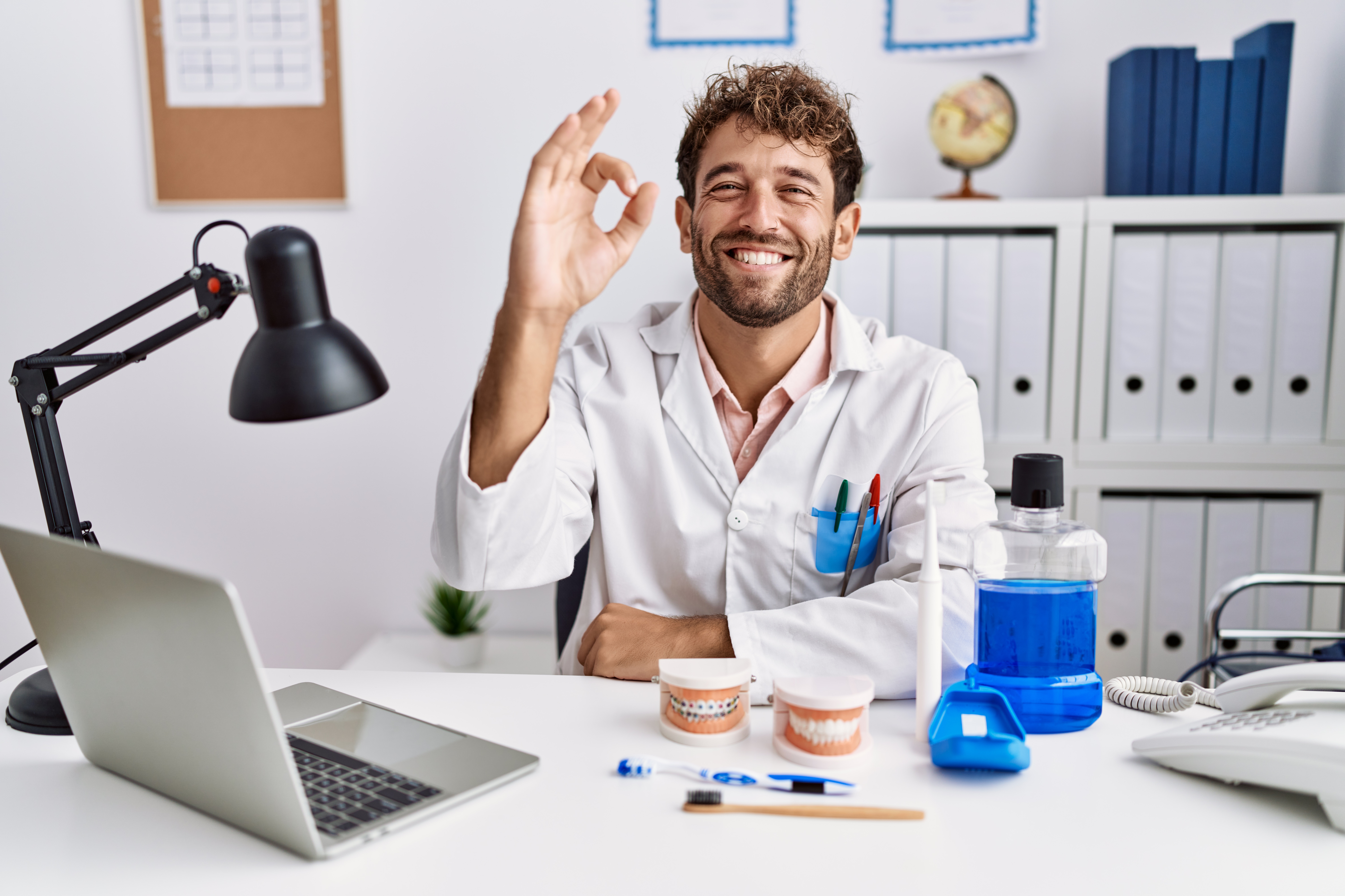young-hispanic-dentist-man-working-medical-clinic-smiling-positive-doing-ok-sign-with-hand-fingers-successful-expression