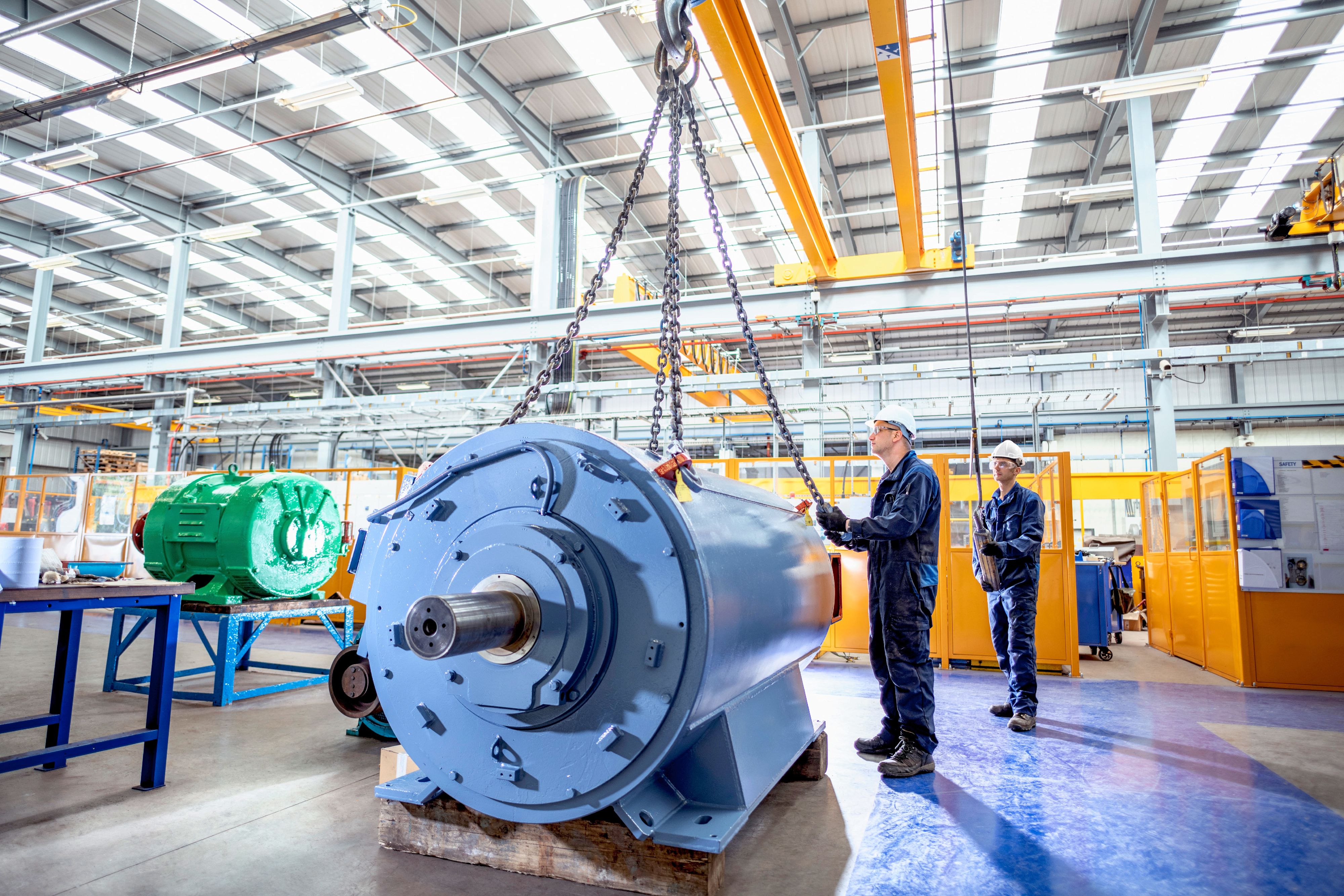 Due collaboratori spostano un grande motore elettrico con un carroponte in un moderno stabilimento produttivo.