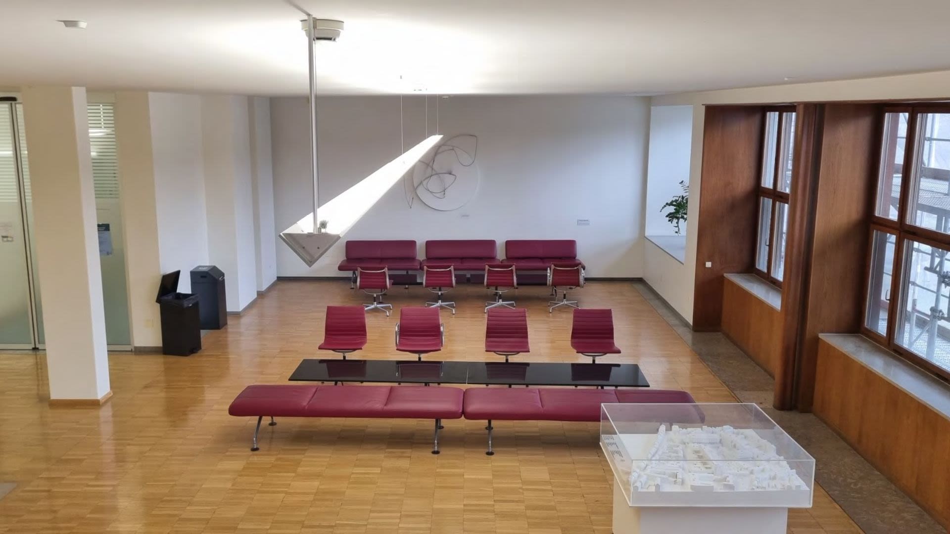 Sala d’attesa Unispital Basel: Ambiente luminoso con sedute rosse, pavimento in legno e grandi finestre.
