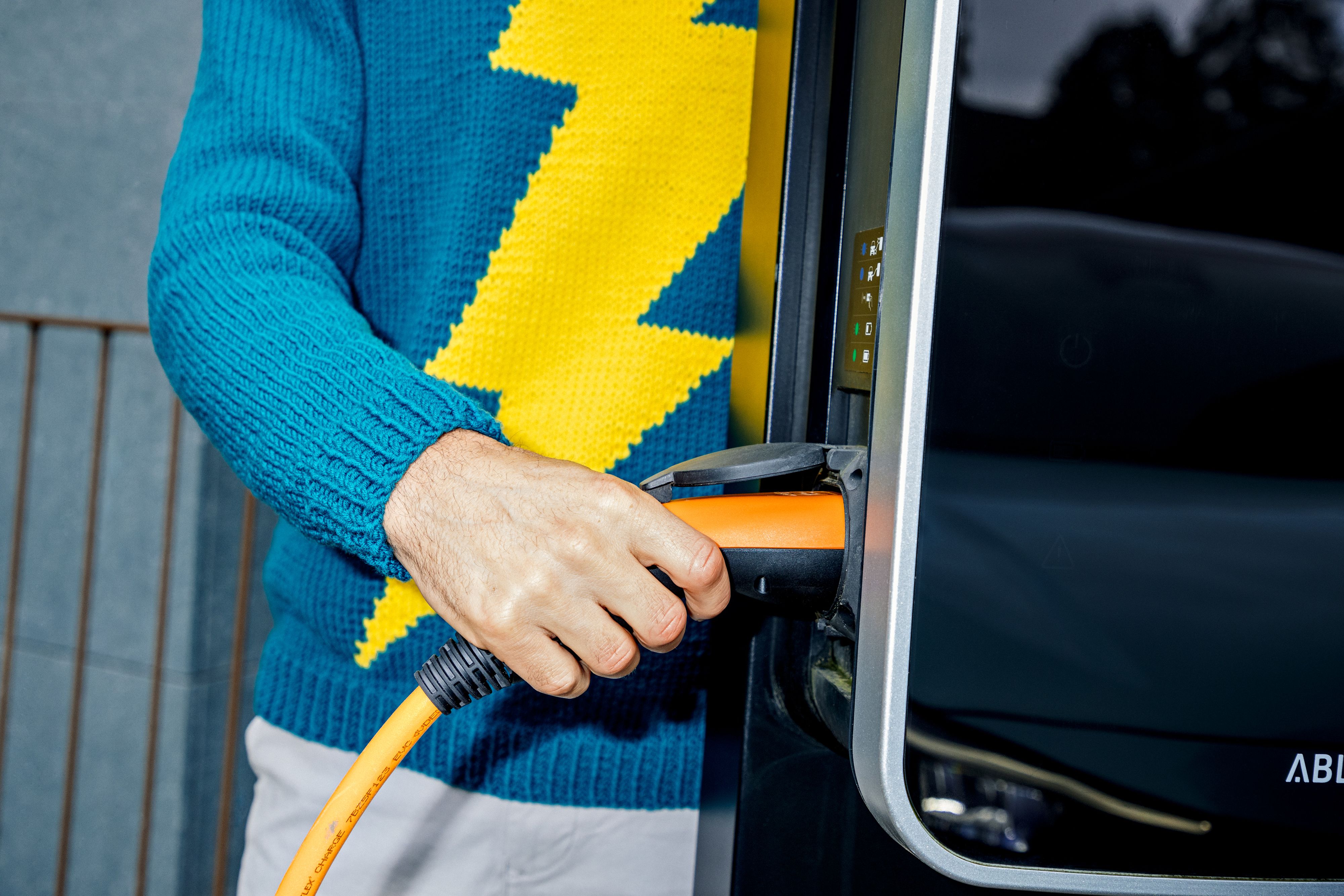 Mann mit Blitzpulli lädt E-Auto