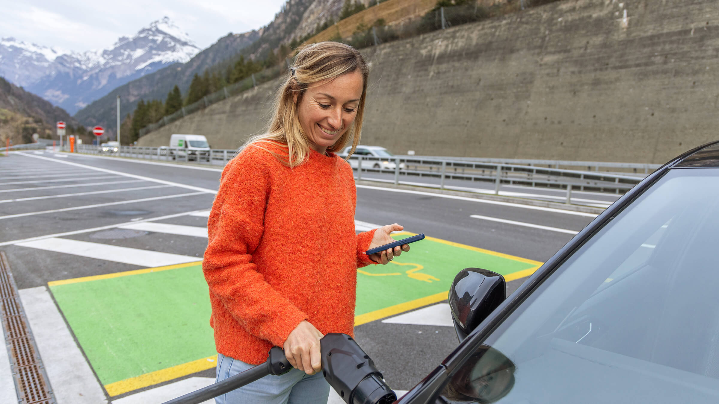 Eine Frau, die ihr Elektroauto an einer Autobahnraststätte in der Schweiz an die Ladestation anschliesst