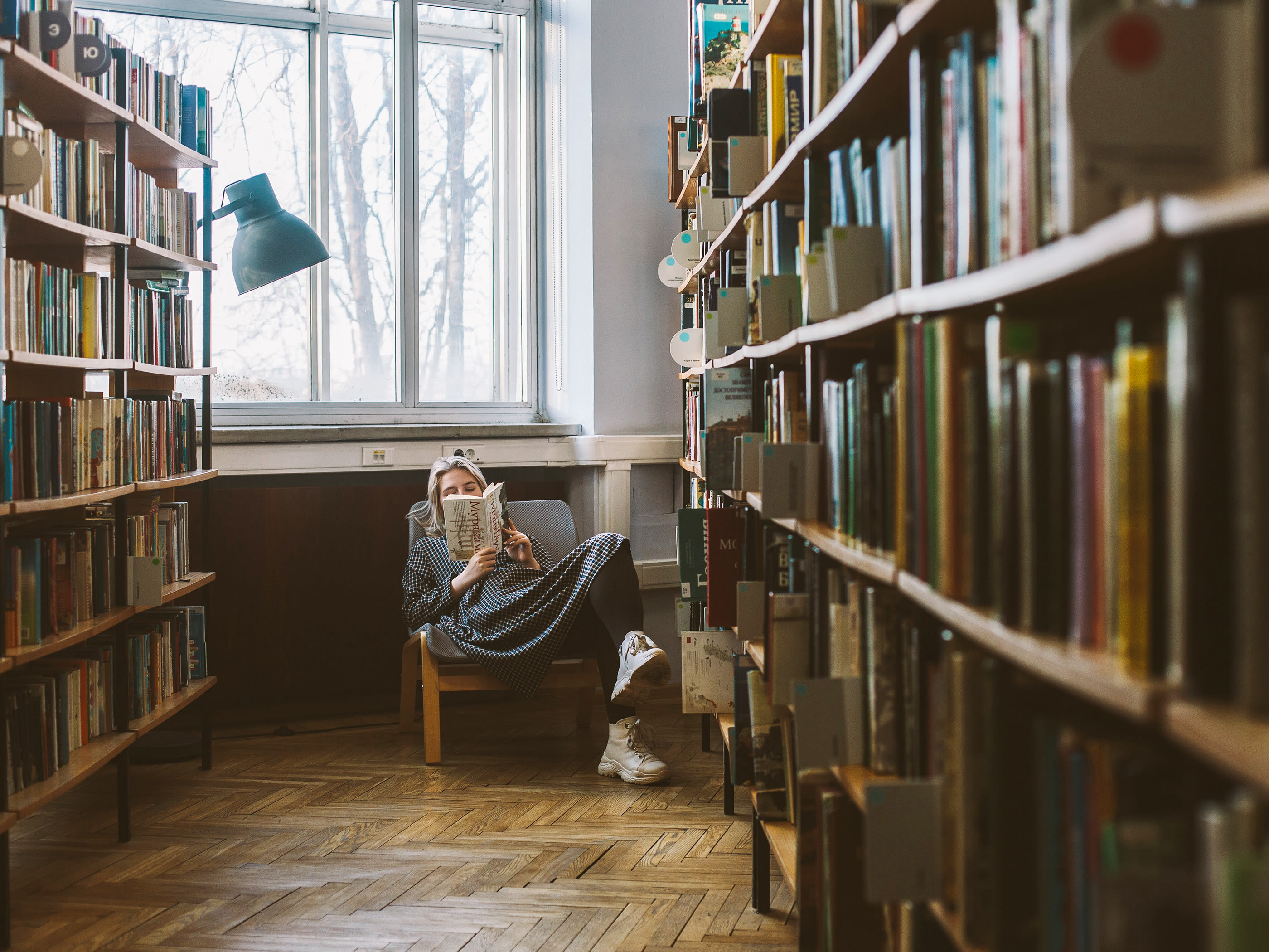 Eine Frau sitzt im Sessel einer Bibliothek und liest ein Buch.
