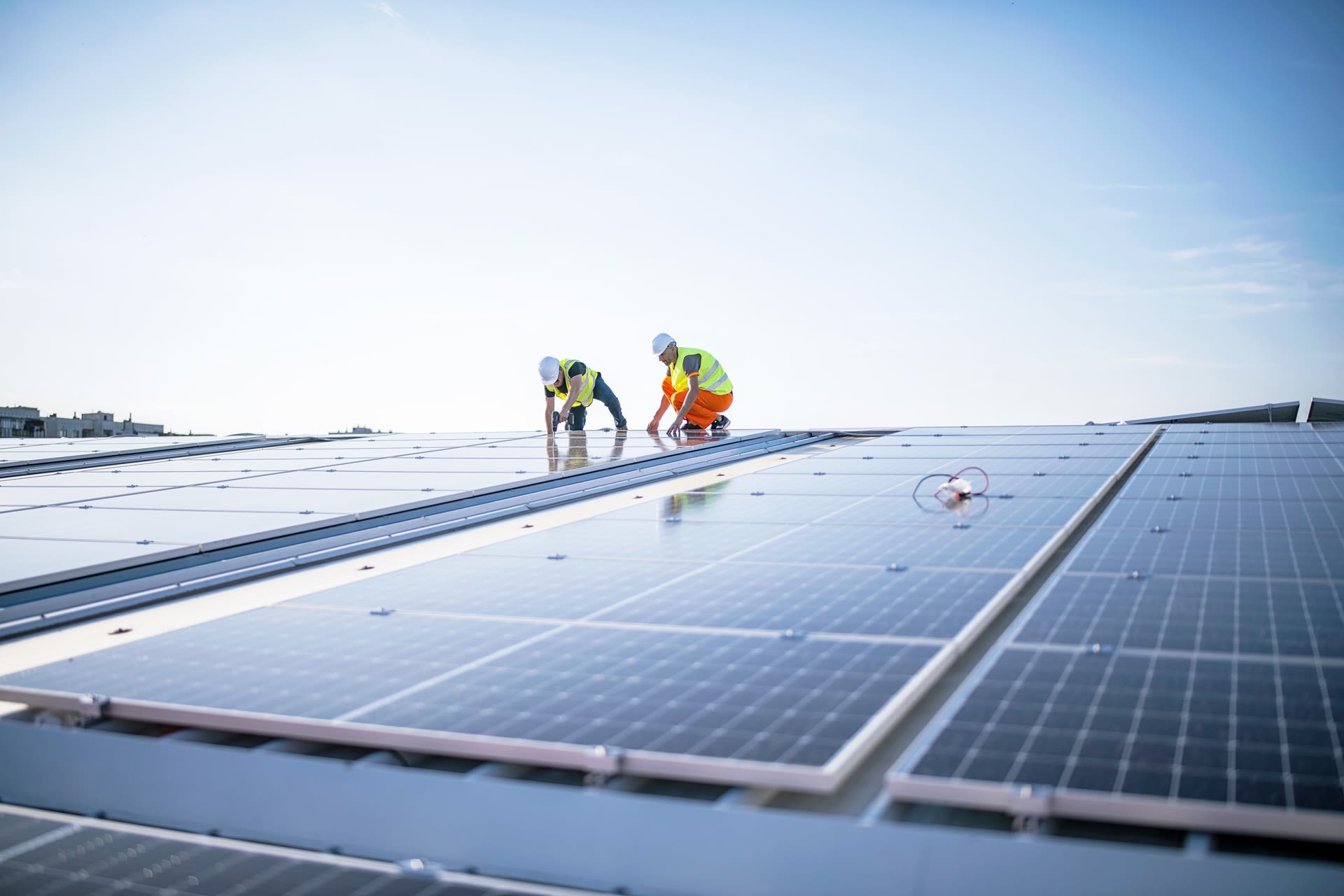 Zwei Fachkräfte installieren und prüfen eine Photovoltaikanlage auf dem Dach eines Industriegebäudes.