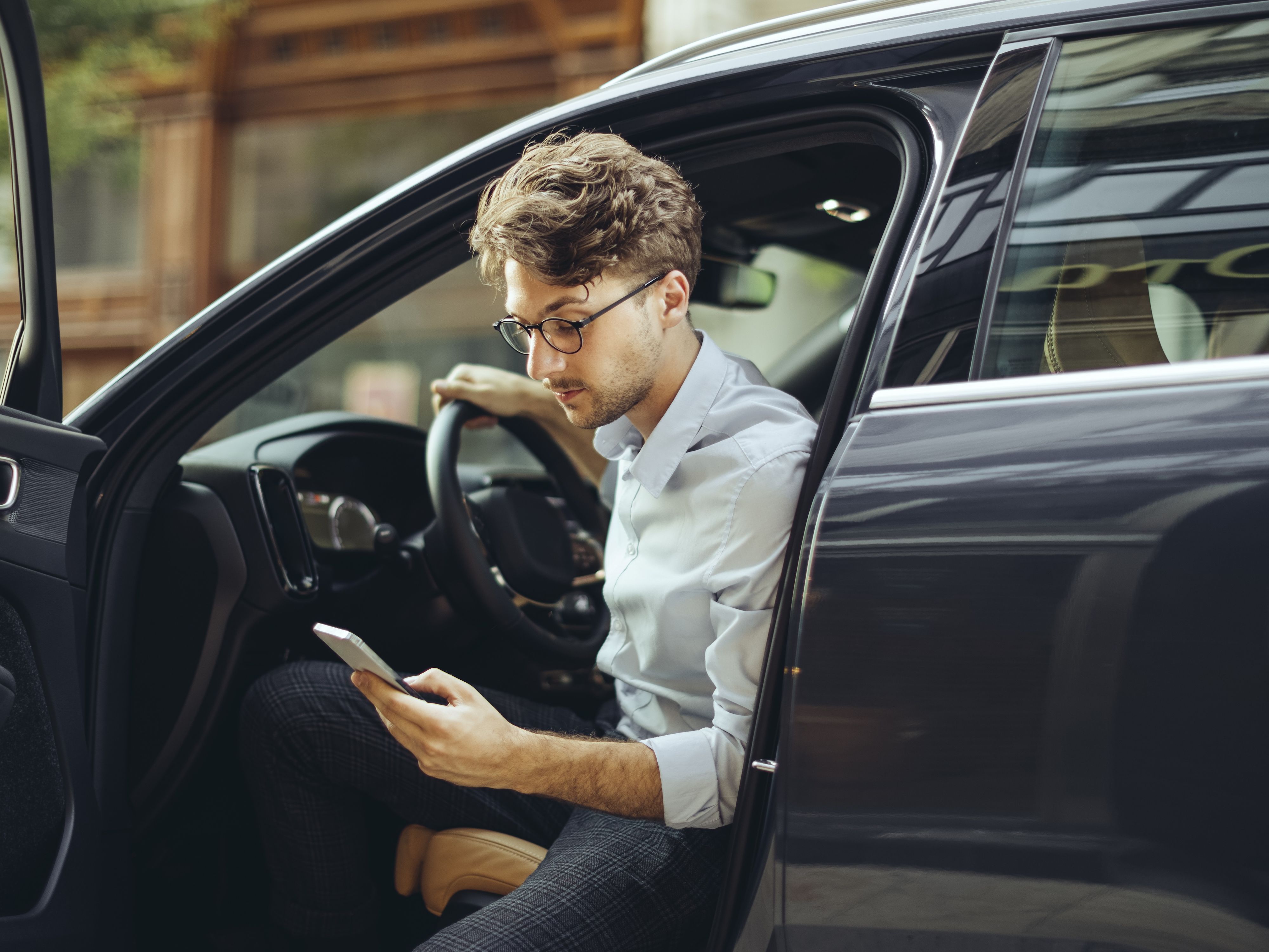 Un uomo con uno smartphone in mano scende da un'auto elettrica