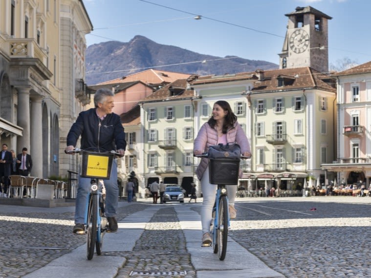 Une femme et un homme traversent Locarno à vélo.