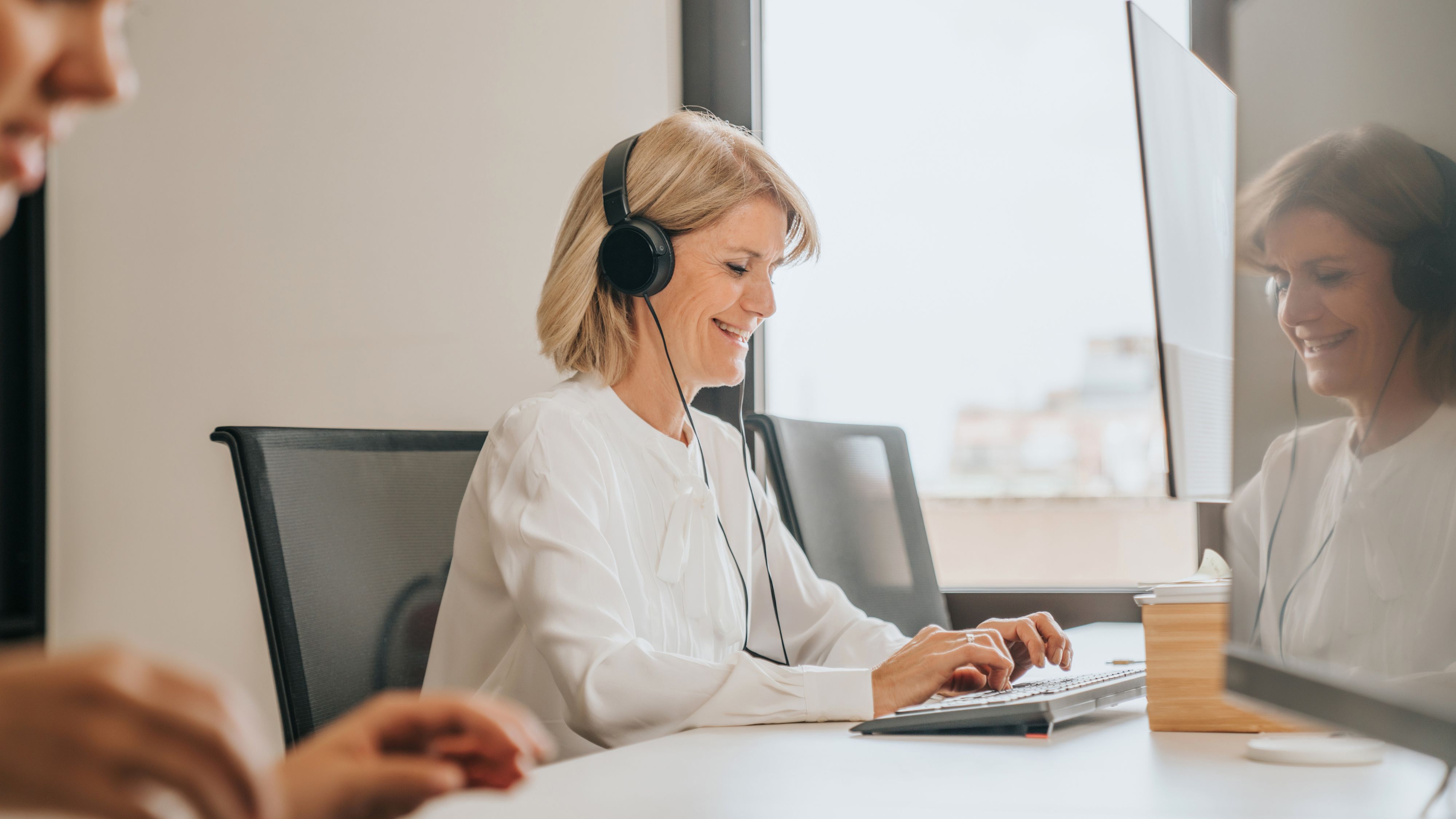 Une femme est assise devant son ordi avec des écouteurs et tape sur le clavier.