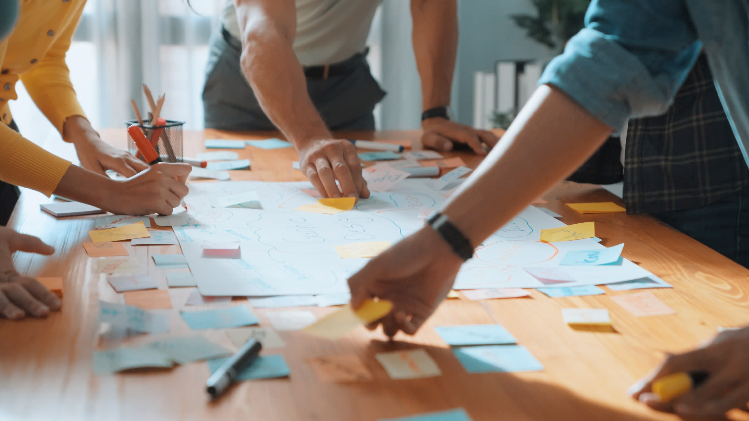 Un team che fa brainstorming attorno a un tavolo attaccando post-it su un grande foglio