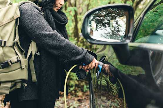 Une femme avec un sac à dos branche le câble de recharge à la voiture électrique.